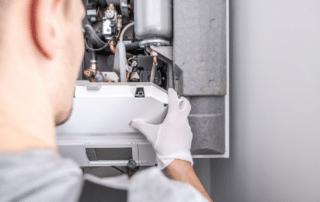 A man in a white shirt and gloves repairs a heat pump, showcasing expertise in heat pump installation in Utah.