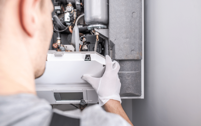 A man in a white shirt and gloves repairs a heat pump, showcasing expertise in heat pump installation in Utah.